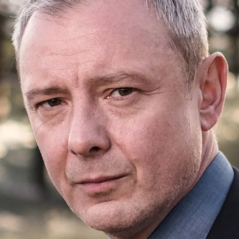 A person from The Print 4 Team, with short gray hair, wearing a suit, looks seriously towards the camera.