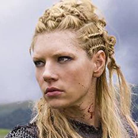 A person with braided blonde hair in medieval attire stands serious against a cloudy sky, as if posing for The Print 4 Team's historical collection.